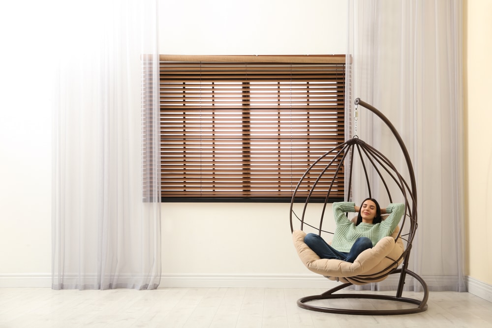 Young woman relaxing in hanging chair near window at home