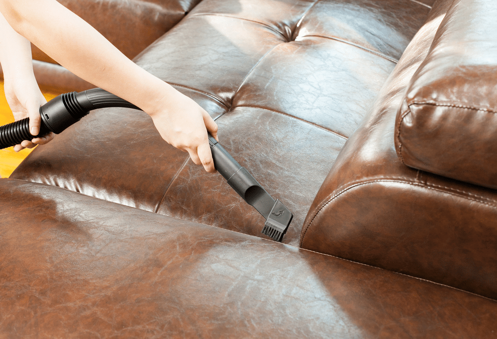 woman cleaning leather sofa with vacuum cleaner