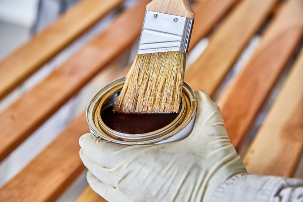 Man's hand holding a can of clear coat wood varnish to treat birch wood slats