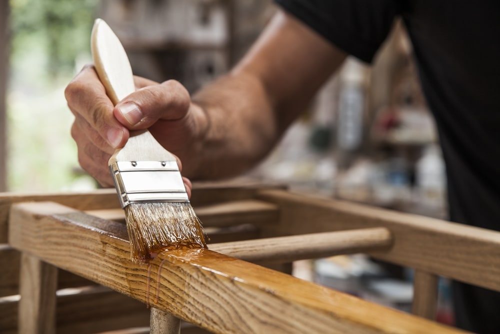 Hand Holding A Brush Applying Varnish Paint On A Wooden