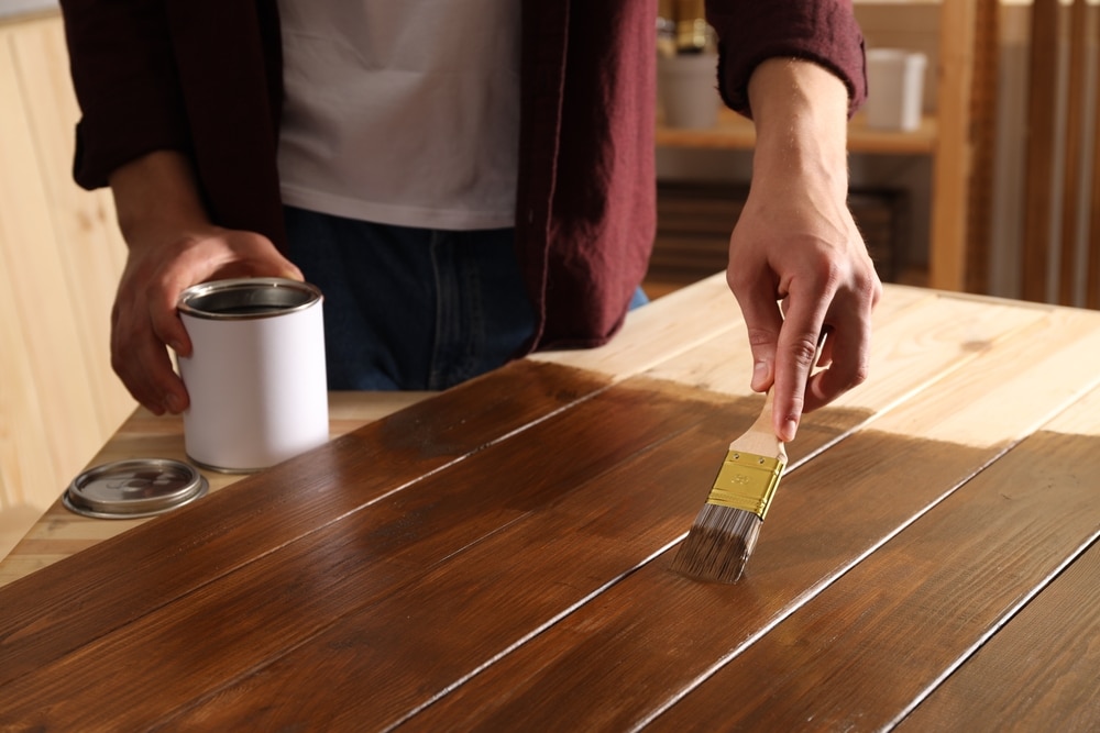 Man With Brush Applying Wood Stain Onto Wooden Surface Indoors