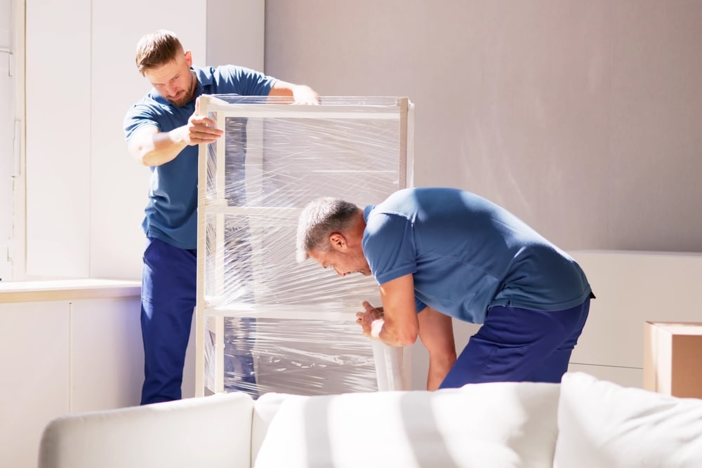 Professional Movers Wrapping Furniture While Moving House